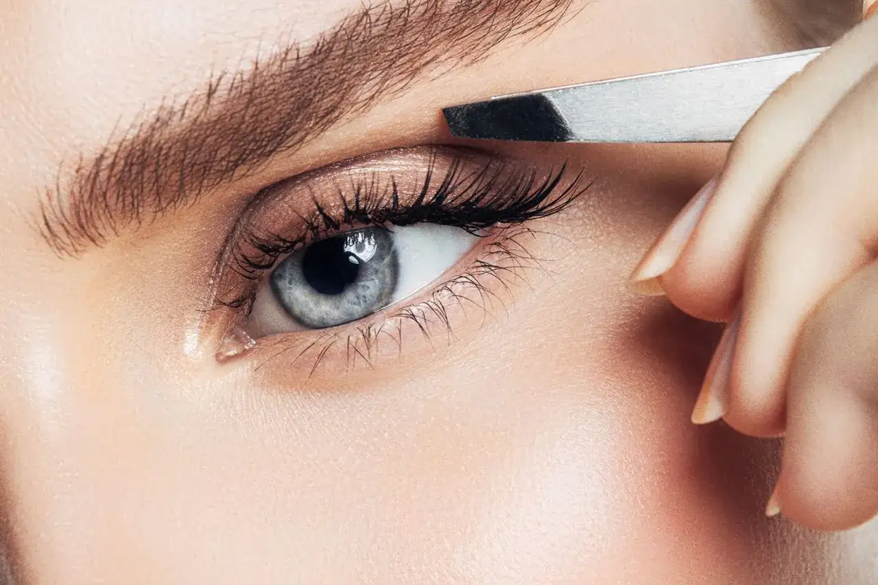 Une main utilise une pince à épiler pour parfaire un sourcil. Quelle pince à épiler choisir pour un résultat impeccable ?