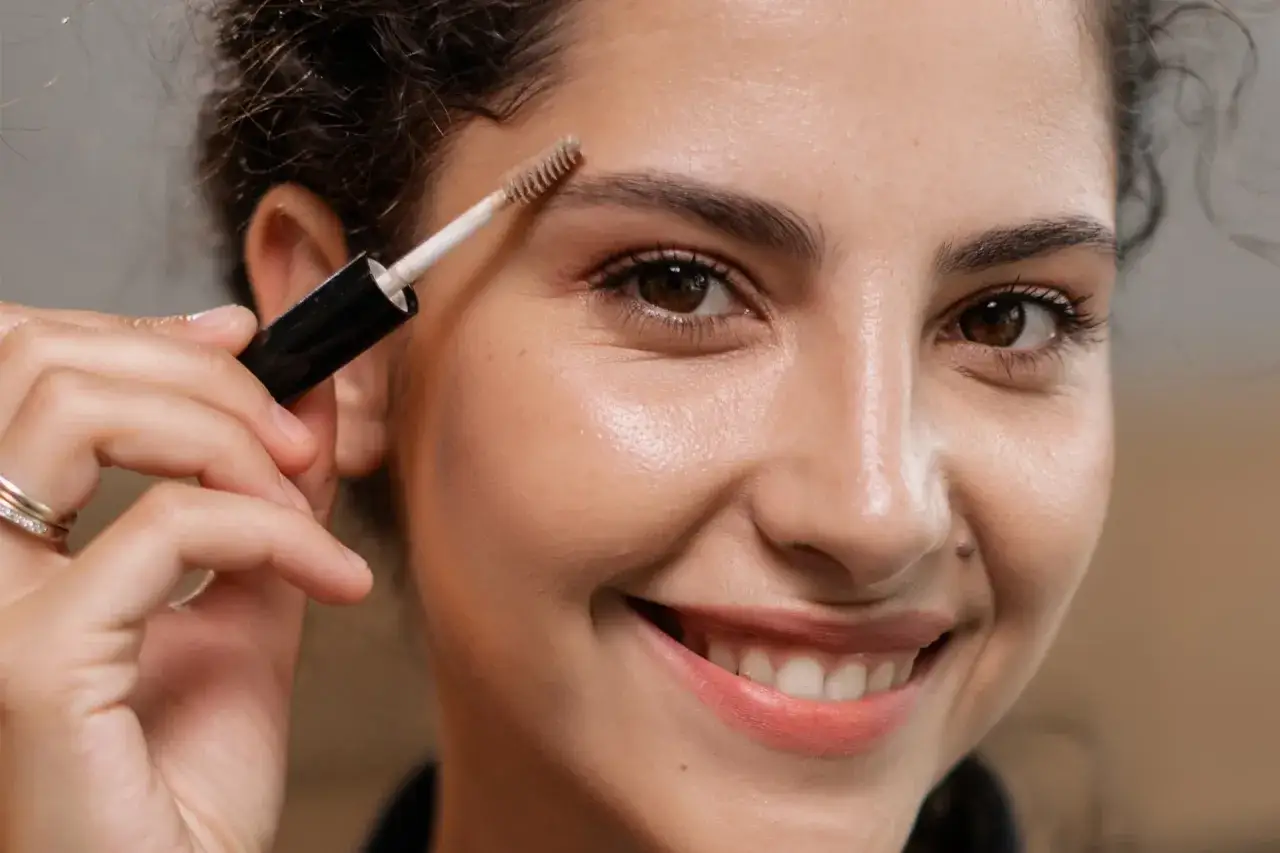Une femme souriante utilise une brosse pour teindre ses sourcils.