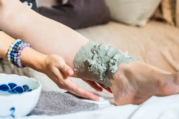 Application d'un cataplasme d'argile verte sur une jambe, pour un soin détoxifiant et apaisant.